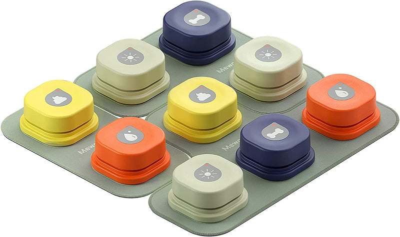 A set of colored communication buttons arranged on a gray mat, each labeled with different icons indicating commands such as food, water, poop, and outside. The buttons are in various colors, including orange, yellow, blue, and gray.