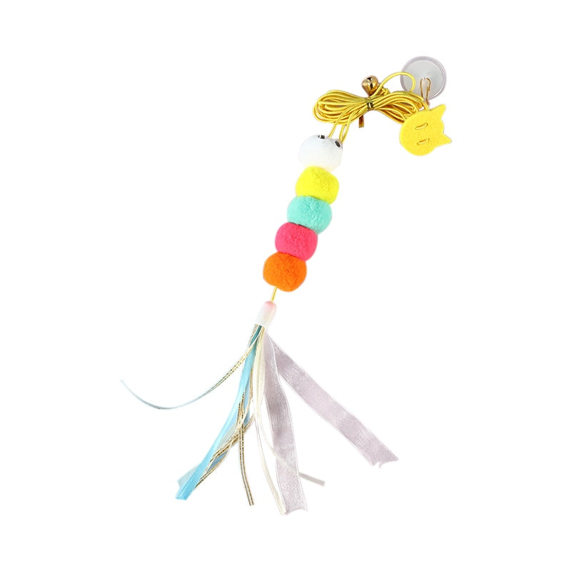 A colorful cat toy featuring five pom-poms in white, yellow, green, pink, and orange, with hanging ribbons. The toy is attached to a yellow string with a suction cup, designed to engage cats in interactive play.