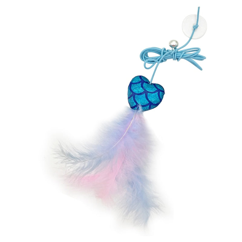 A cat toy featuring a blue heart-shaped center with a fish scale pattern and pastel pink and blue feathers. The toy is attached to a blue string with a suction cup for easy attachment to surfaces, designed to entertain and engage cats.