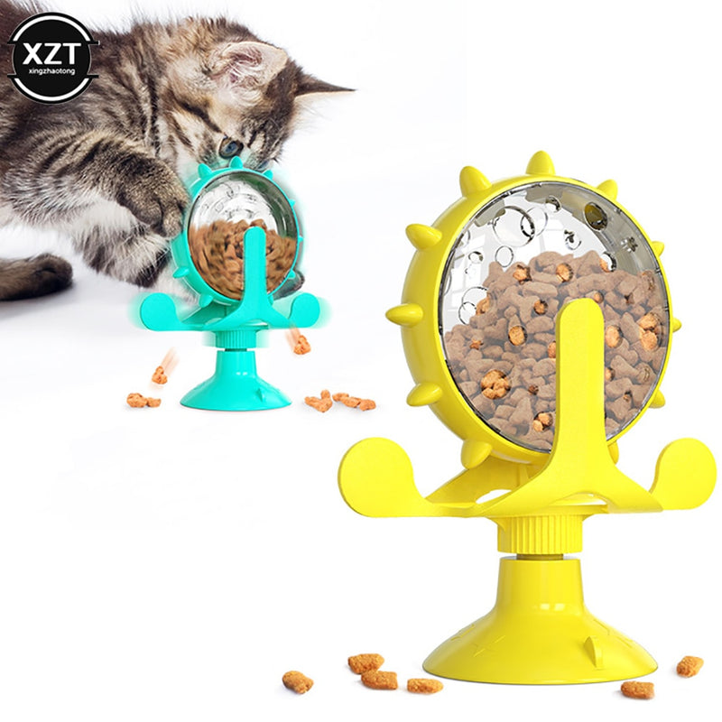 A fluffy kitten plays with a turquoise treat-dispensing toy, while a similar yellow toy is shown beside it. Both toys have a spiked, clear globe filled with treats and a suction cup base, designed to provide interactive fun for cats.