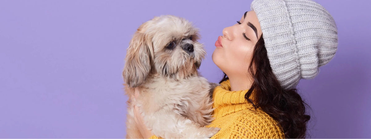 A woman carying a yorki and about to give him a kiss on the cheek