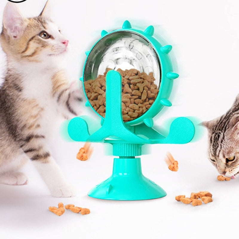 Two kittens interact with a turquoise treat-dispensing toy that features a spiked, clear globe filled with treats. The toy has a suction cup base and is designed to rotate and release treats as the cats play with it.